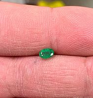 Close-up of emerald resting on fingertip showing size and color