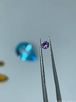 Purple round sapphire held by tweezers with other gems blurred in background