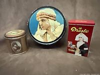 Group shot of three advertising tins: Beautebox round tin, Coca-Cola round tin, Droste rectangular tin