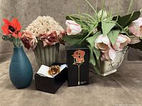 Group shot showing all items: teal vase with poppies, fluted planter with roses, white planter with tulips, boxed gold rose brooch