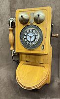 Front view of wooden wall phone showing bells, dial, handset, and lower compartment