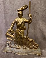 Front view of gilt cast iron Scottish Highlander soldier doorstop showing detailed attire, staff and rocky base