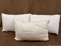 Front view of three white accent cushions showing two matching scroll-quilted designs and one hexagon-quilted design
