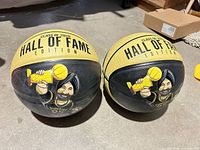 Two yellow and black Nav Bhatia Hall of Fame Edition basketballs laying on floor showing graphics and wear