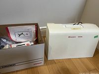 Sewing machine hard case beside box of accessories