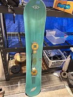 Full view of teal-green Killer Loop snowboard with bindings attached