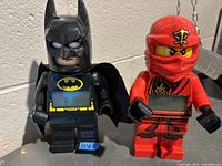 Front view of Batman and Red Ninjago digital alarm clocks showing LCD displays.
