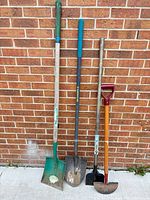 Four garden tools leaning against brick wall full view