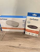 Retail box of Manhattan phone sanitizer with Qi wireless charger alongside Manhattan 10W charging pad box