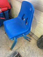 Side view of one blue plastic school chair showing seat, backrest cutouts and metal legs