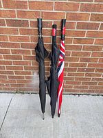 Three umbrellas closed leaning against brick wall showing handles and folded canopies