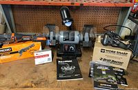 Overall lot showing bench grinder, Ridgid multi-tool, Work Sharp sharpener box, manuals, accessory packs