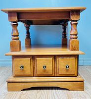 Full view of honey finish Design Inc. side table showing drawer front, turned legs, lower shelf, and plinth base