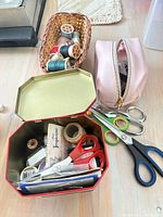 Overall lot showing tin, scissors, basket with thread spools, pink pouch