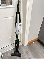 Full view of Bissell MagicVac 2033 stick vacuum standing upright with cord and attached manual