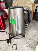 Black+Decker stainless-steel electric kettle showing exterior, handle, water-level window, cord and plug