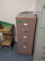Full view of brown 3-drawer metal file cabinet next to other furniture items