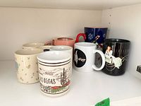 Shelf holding nine assorted ceramic coffee mugs with various colors and graphics