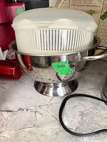 Stainless steel colander containing salad spinner basket and lid, black ring accessory visible