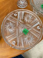 Top view of round clear cut glass platter showing starburst pattern, serrated rim and three ball feet