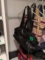 ECCO black leather shoulder bag hanging in closet, front and straps visible