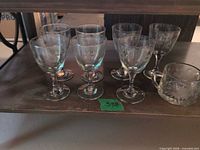 six clear stemmed goblets and handled glass piece on shelf
