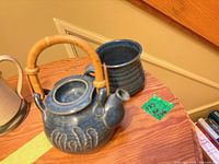 Blue stoneware teapot with lid removed, cane handle, and matching mug on wooden surface
