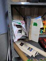 Shelf showing worn Hot Wheels box, white bag with plastic parts, rolled posters and visible colorful Fisher-Price pieces