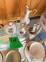 Miniature Limoges porcelain teapot, two ewers, creamer, cup and saucer on glass shelf