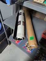 Two rolled posters on shelf, one within cardboard tube, visible automotive text columns