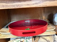 stack of three trays on shelf: red round tray on top, white rectangular tray beneath, cream script tray at bottom