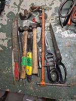 All tools grouped on tabletop: files, hammers, pipe wrench, shears, tin snips, coping saw frame