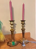 pair of brass candlesticks with pink tapers and silver-tone snuffer on wooden surface