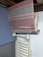 Folded white metal chaise lounger showing pink striped sling seat, beige cushion, white wheels