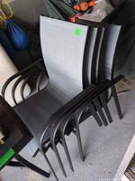 Four stacked black aluminum patio chairs with gray sling seats