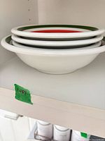 Stack of four white ceramic pasta bowls with colored rims on shelf