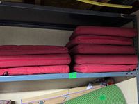 Eight red patio seat cushions stacked on a shelf; four of these constitute the lot