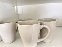 Four white tapered ceramic mugs on shelf