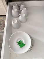 Six upside-down white porcelain cups and stack of six saucers