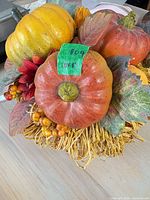 Top view showing three artificial pumpkins/gourds, fabric leaves, berries, red flower and raffia base
