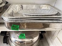 Stainless roasting pan with stacked disposable aluminum pans on shelf