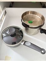 Overhead view of two T-fal saucepans and single glass lid