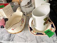 Creamer on saucer next to scalloped floral bowl