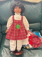 Full view of doll on stand with primary outfit and extra clothing pieces beside