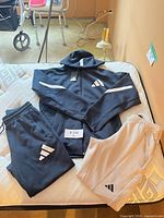 All three Adidas clothing items laid out: navy hooded jacket, navy pants, grey pants