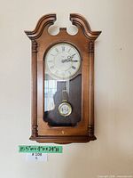 Frontal view of Howard Miller wall clock displaying dial, pendulum, wood case