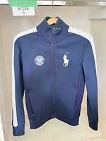 Front view of navy Wimbledon track jacket hung on hanger showing chest patch and Polo Pony logo