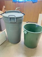 Gray Rubbermaid trash can with lid next to green liner