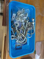 Overview of blue bin showing various U-bolts, eye bolts, washers, nuts and strap