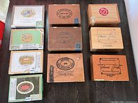 Top view of all ten wooden cigar boxes showing assorted brand graphics and condition